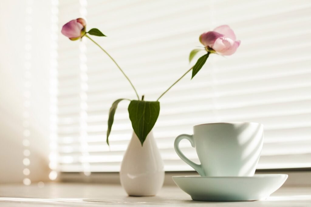 flower-vas-coffee-cup-with-saucer-near-window-blind_23-2148209293